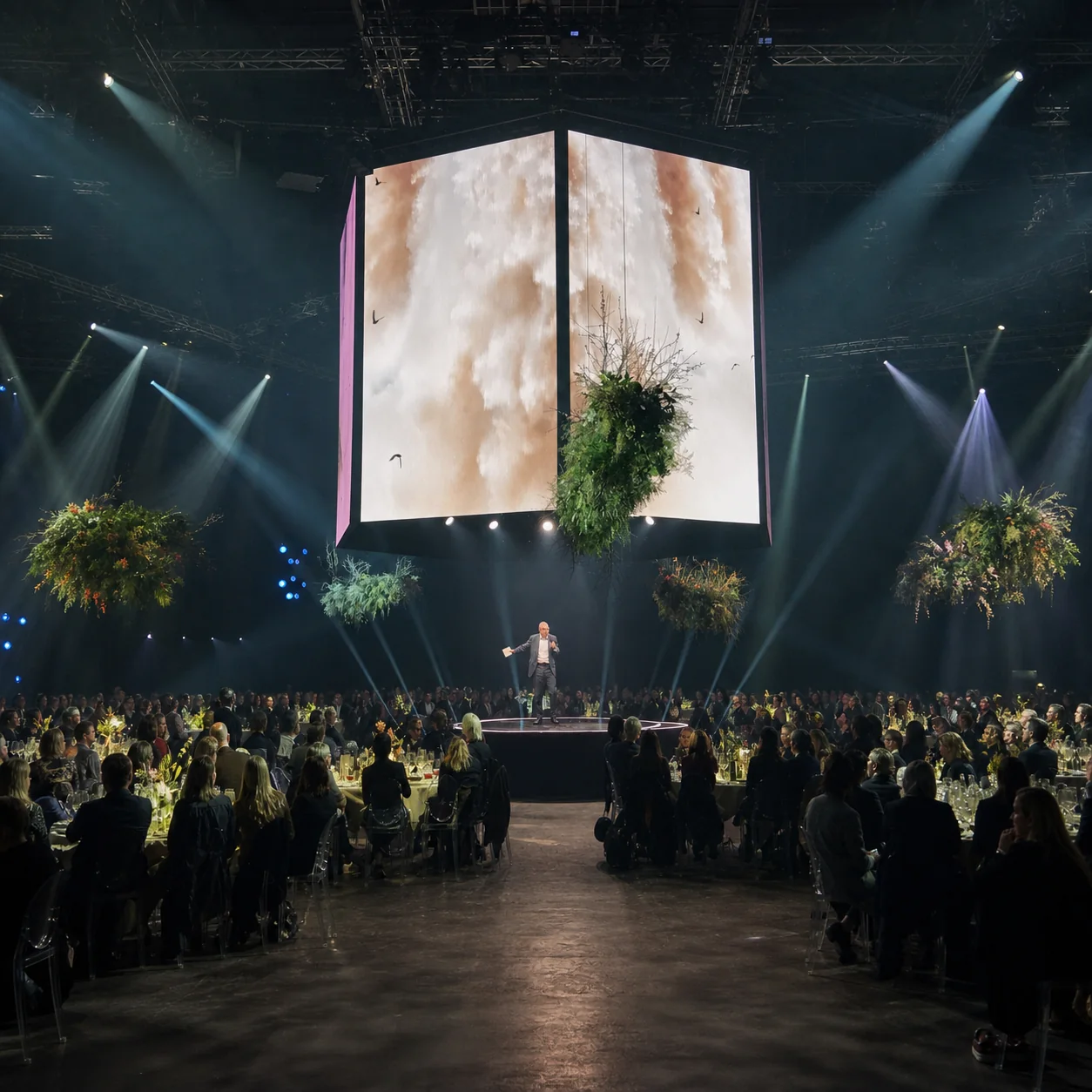 A presenter beneath a suspended screen installation at a global media showcase
